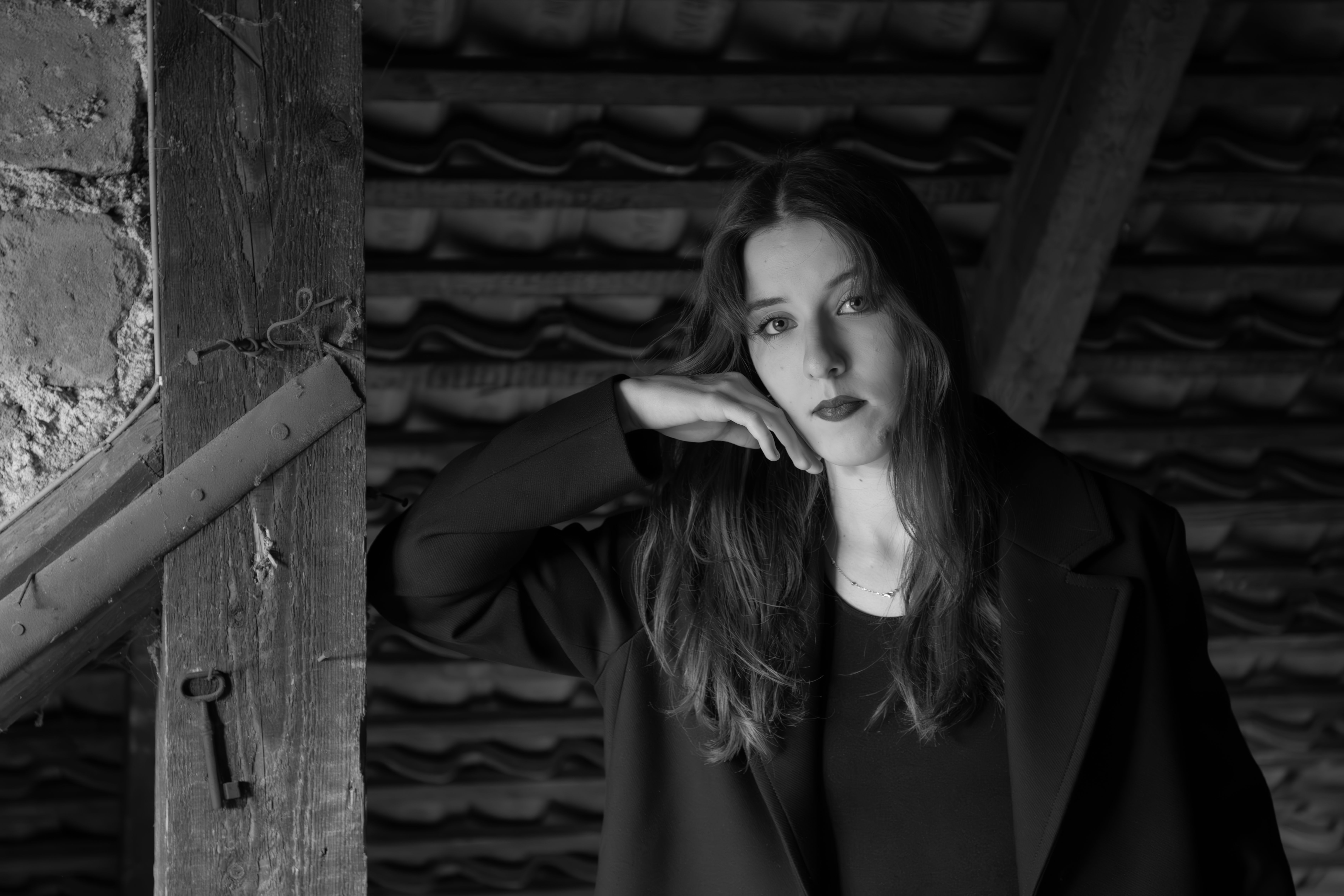 A thoughtful woman in black and white, posing indoors with a rustic background.