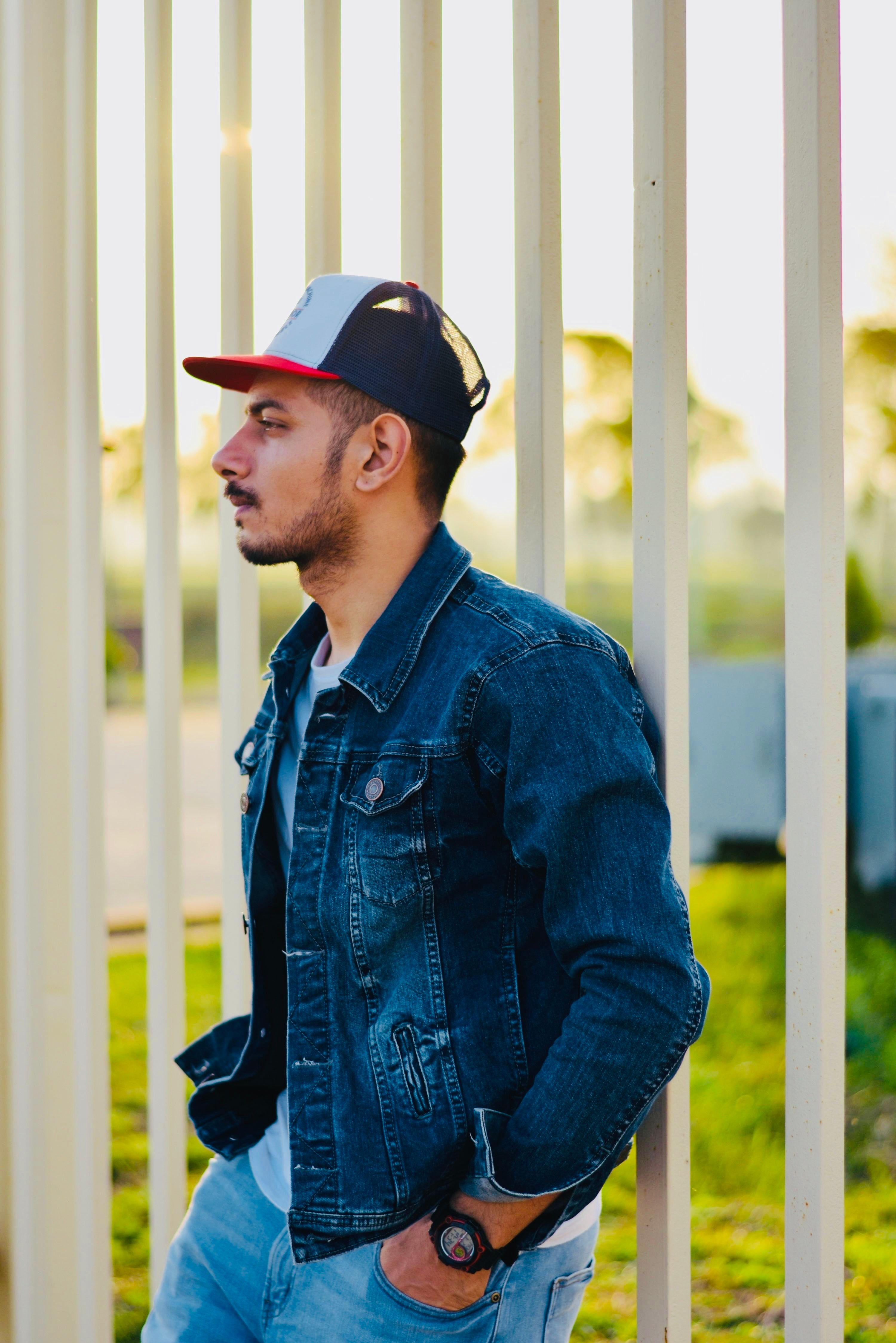 Man in denim jacket and cap leans on railing during a vibrant evening in India.