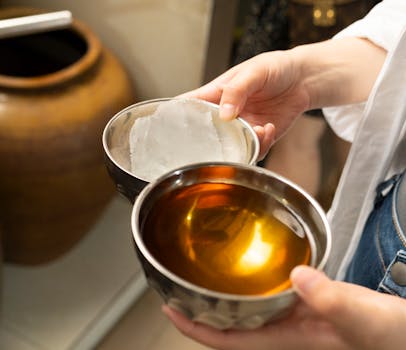 Close-up of traditional Yunnan cuisine preparation in China, featuring hands holding metal bowls.
