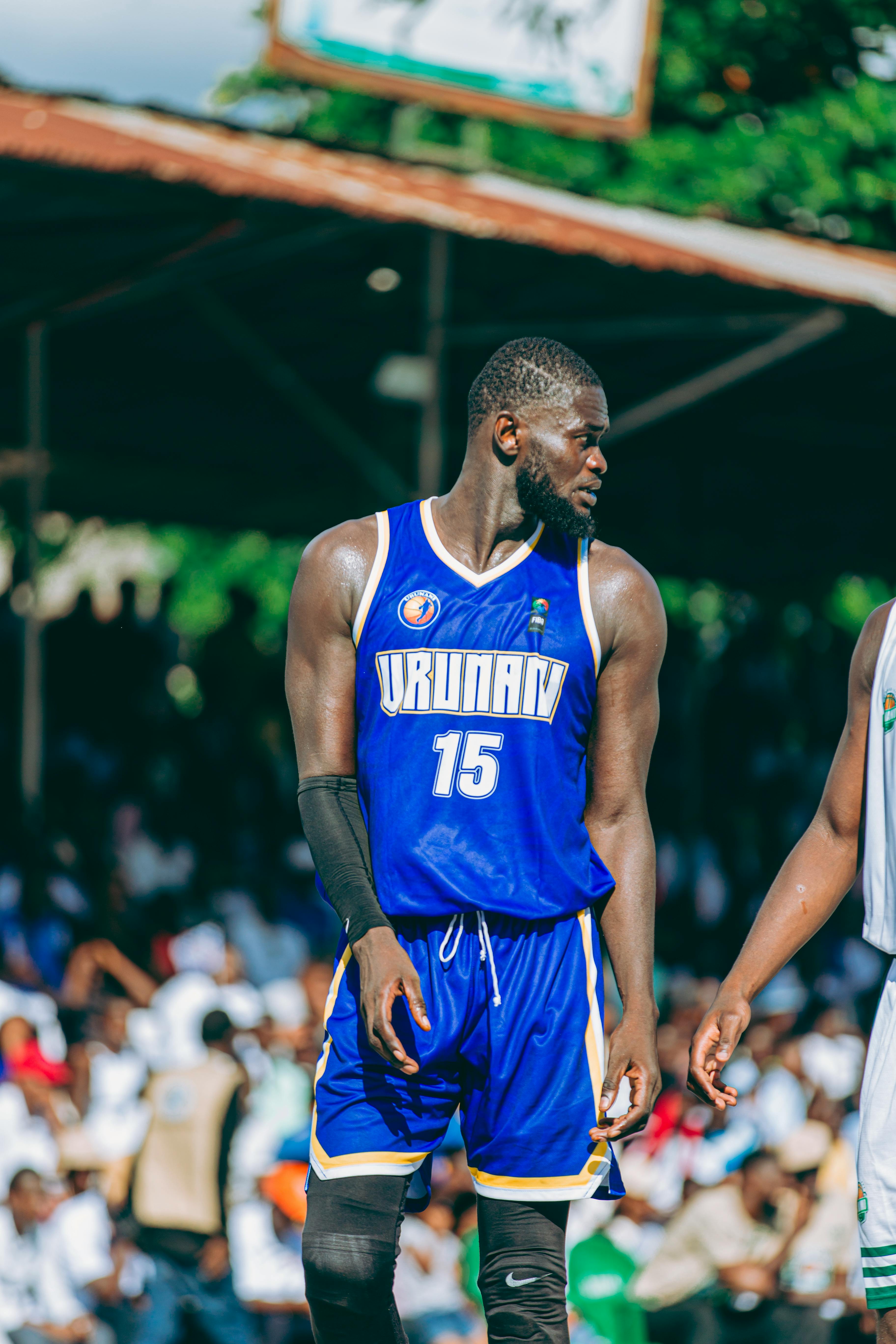 Basketball player in blue jersey during outdoor game with spectators and greenery in background.
