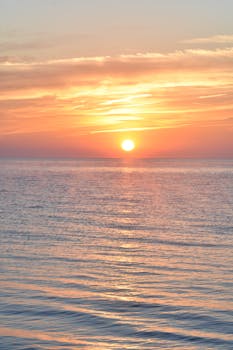 Peaceful sunrise over the ocean with vibrant orange and pink hues reflecting on calm waters.