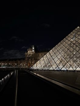 Night view of the Louvre Museum and its iconic illuminated glass pyramid in Paris, France.