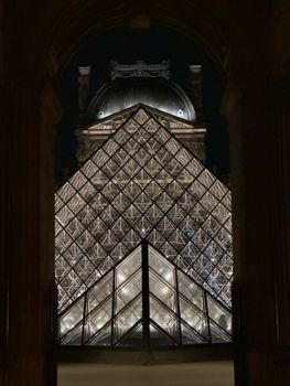 Dramatic view of the illuminated Louvre Pyramid against the night sky in Paris.