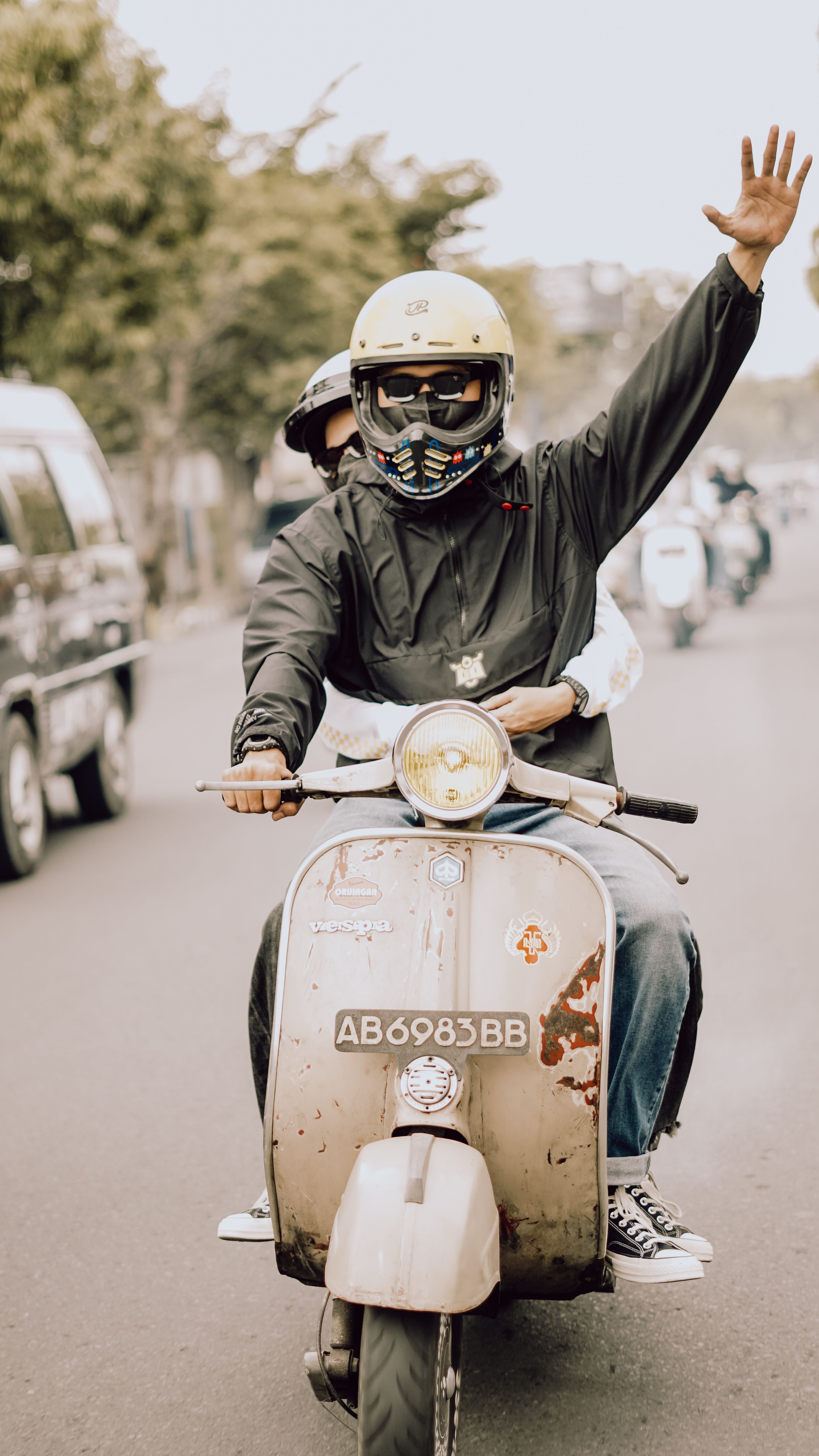 Two people cheerfully riding a vintage Vespa scooter in East Java, Indonesia.