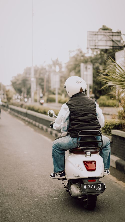 Free Person riding a Vespa scooter on a city street in East Java, Indonesia. Urban lifestyle captured from behind. Stock Photo