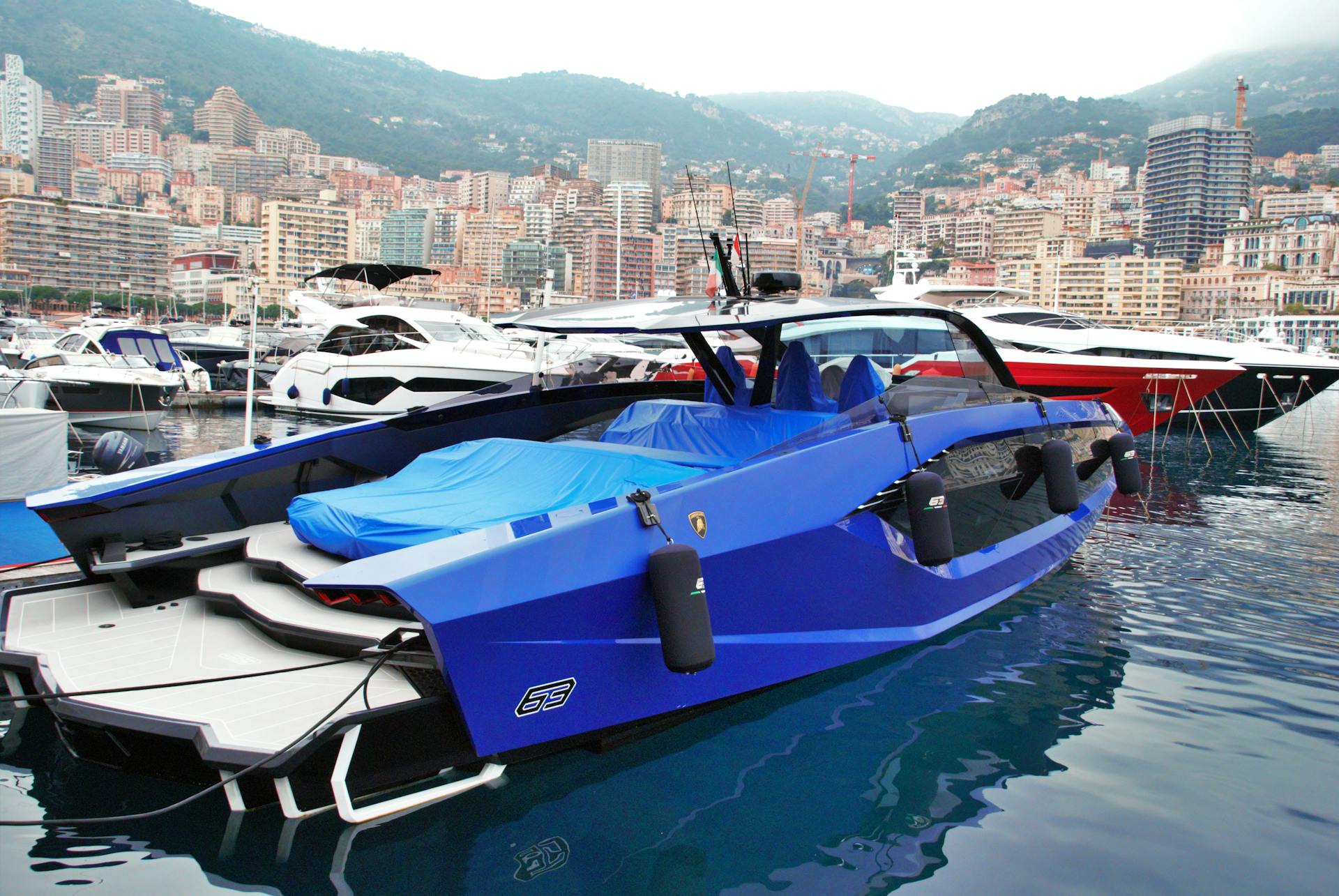 Explore the stunning view of a luxury blue yacht docked in Monaco's scenic harbor with city skyline backdrop.