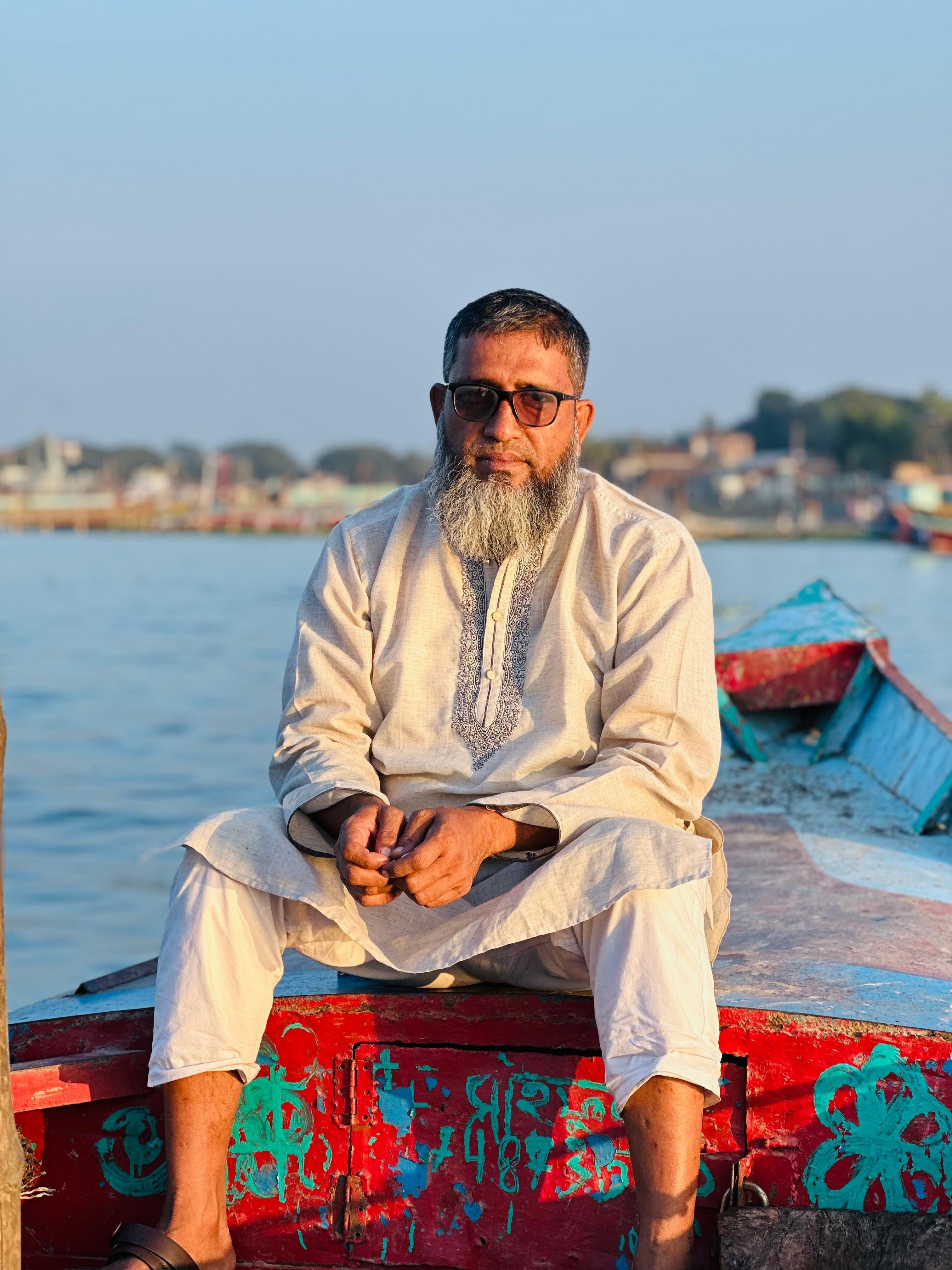 An elderly man sits on a colorful boat by the sea in Mdina, Malta, wearing traditional attire.