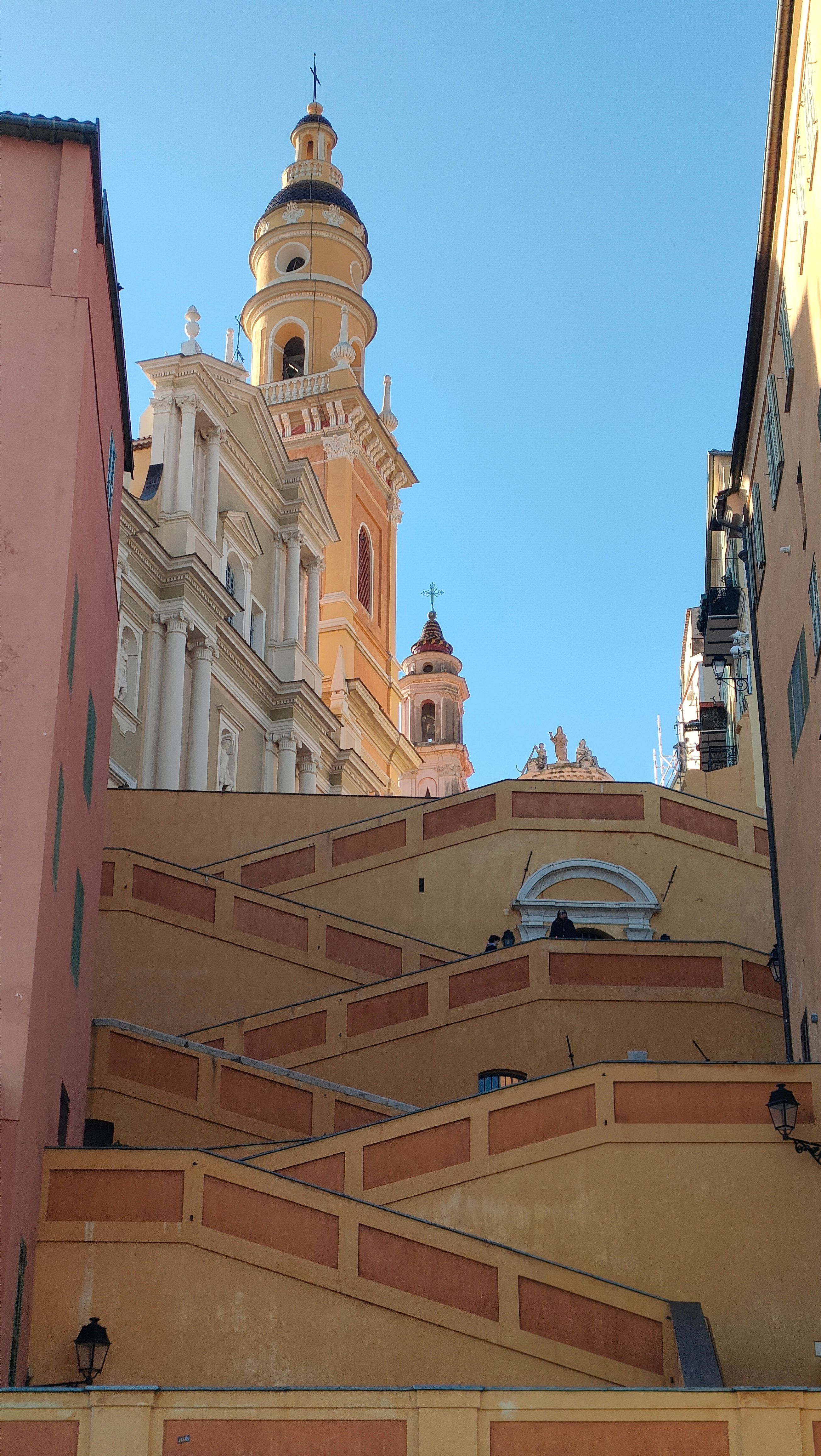 Capture of vibrant buildings and stairs under a bright blue sky in Menton, France.