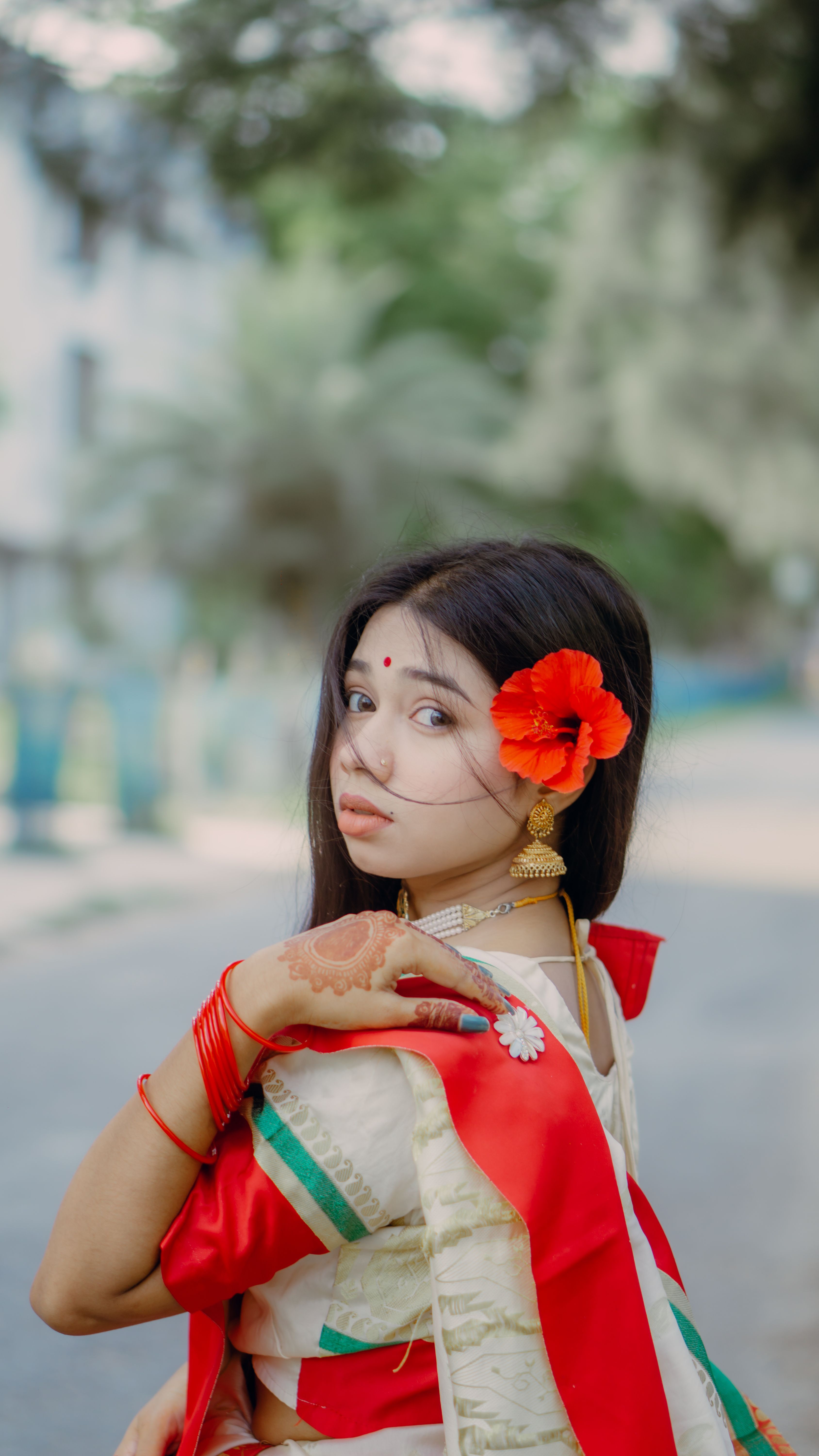 A young woman in a traditional sari adorned with a vibrant flower, looking back over her shoulder.