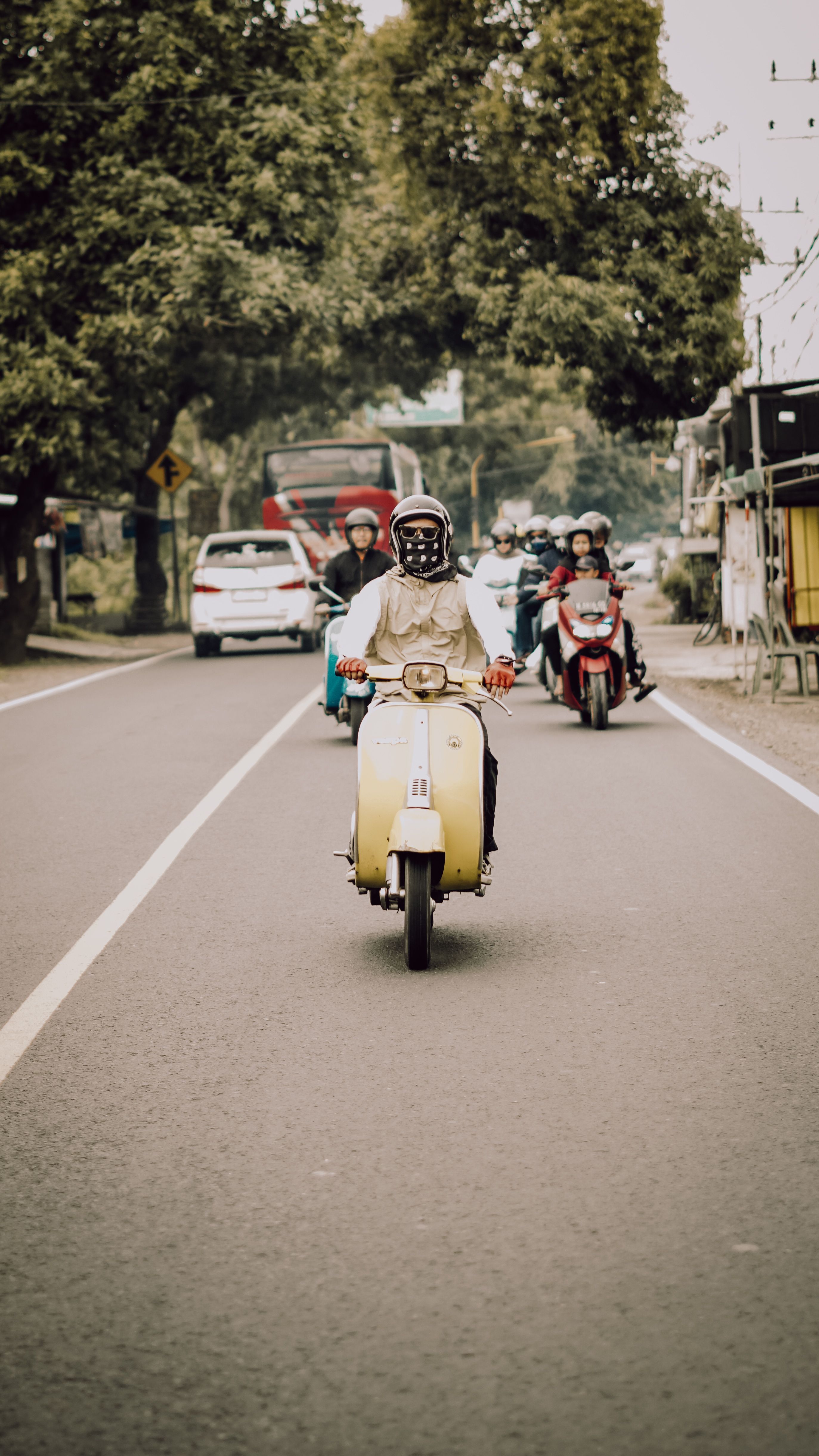 A group of people riding Vespas down a scenic road in East Java, Indonesia.