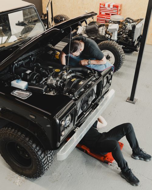 Free Two mechanics repairing a black off-road vehicle in a garage, focusing on engine work and maintenance. Stock Photo