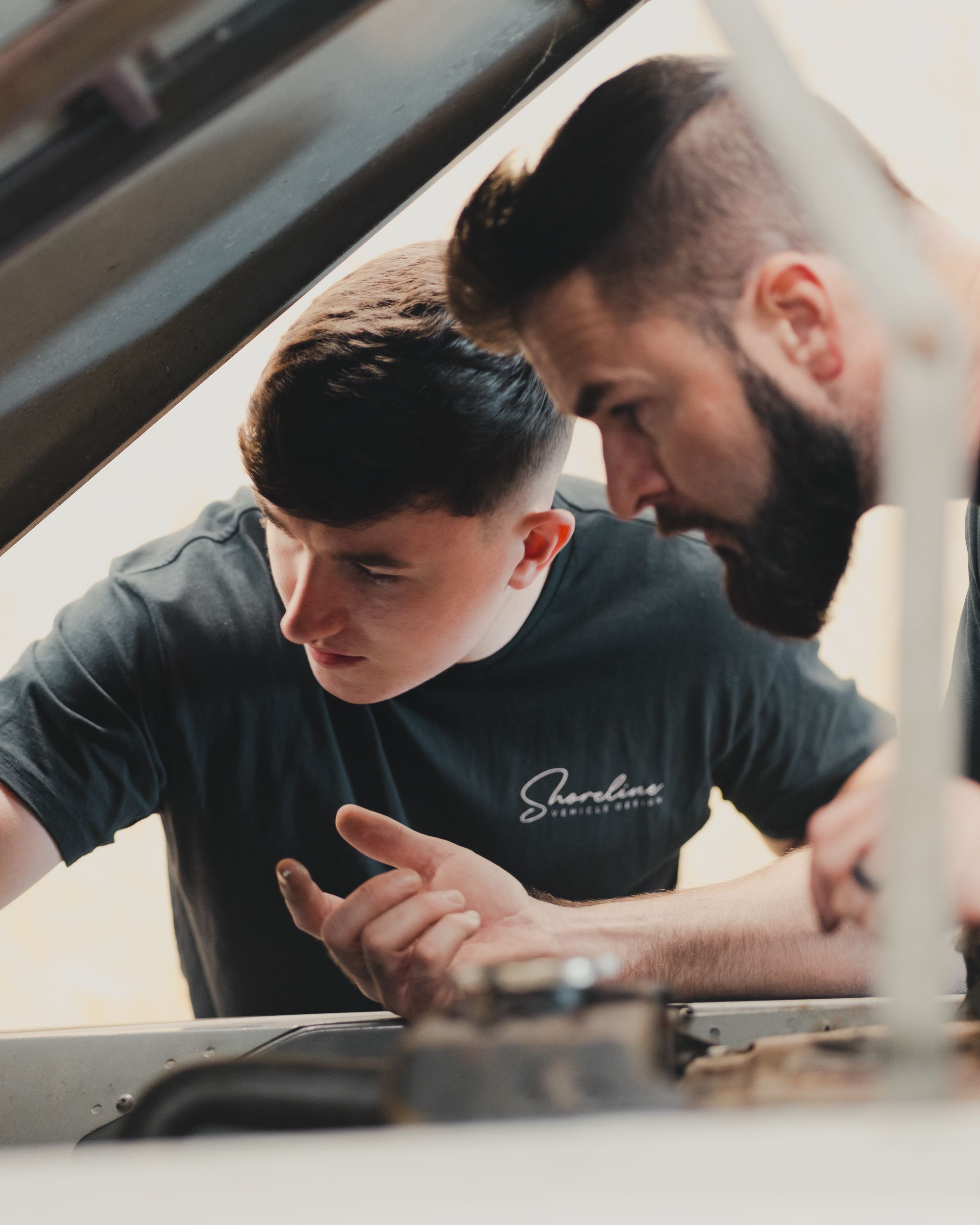 Father and son team working together under the hood of a car, demonstrating teamwork and bonding.