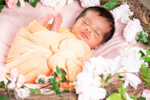 A serene sleeping baby wrapped in orange, surrounded by flowers in Bengaluru, India.