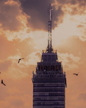 Torre Latinoamericana silhouetted at sunset in Mexico City, with birds flying nearby.