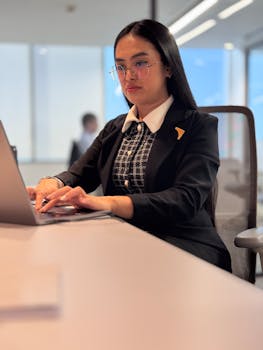 Confident woman in business attire working on a laptop at a modern office desk.