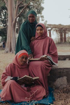 Three women in traditional attire reading books outdoors, showcasing cultural and educational engagement.