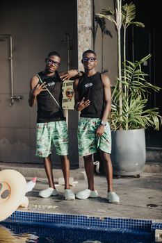Two young men wearing matching shorts and sunglasses standing by a pool.
