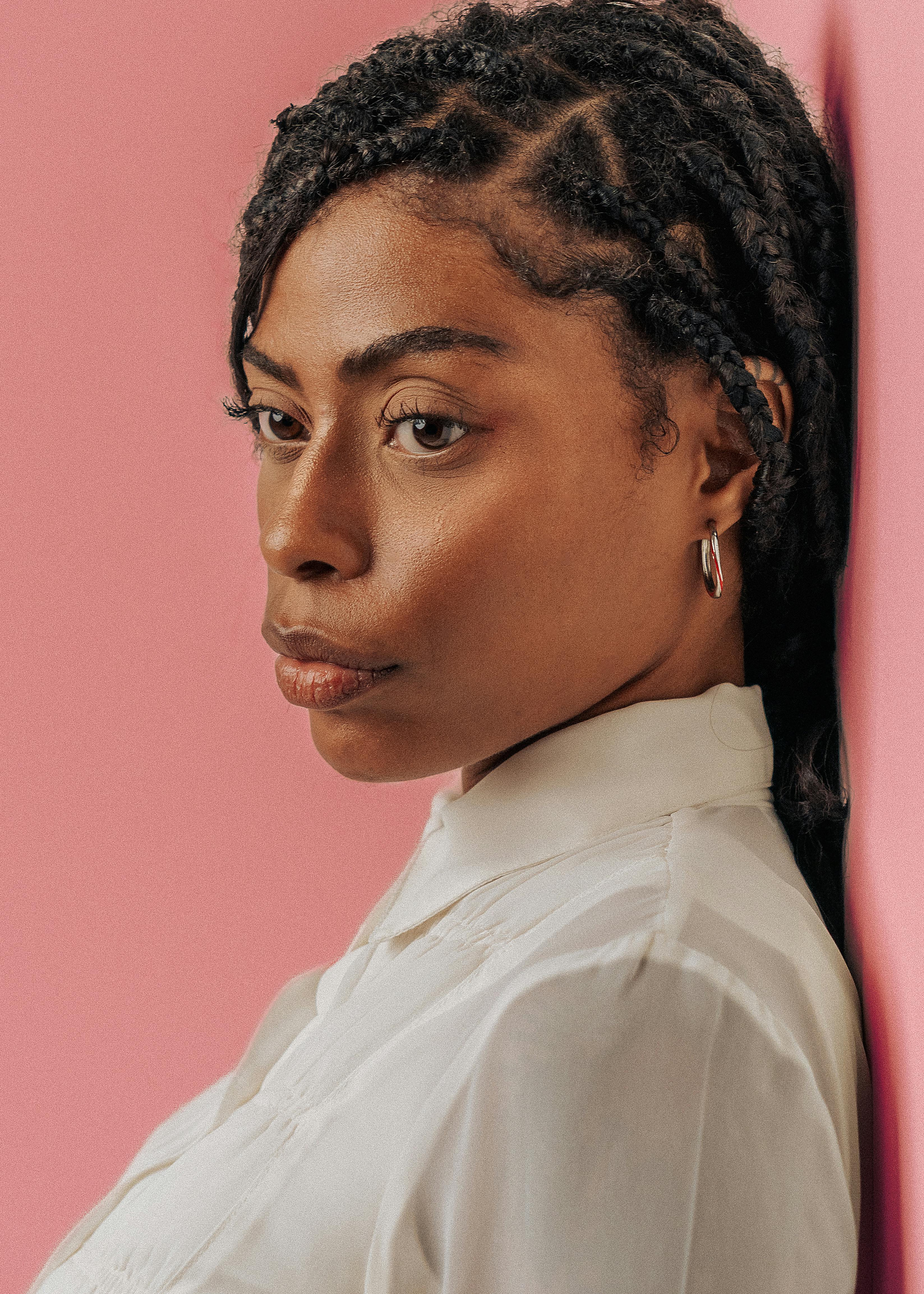 Profile portrait of an African woman with braided hair against a pink wall.