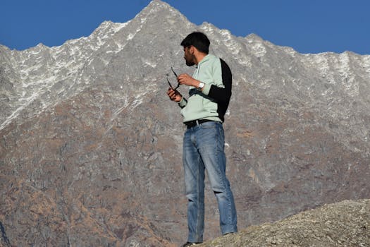 Man controls a drone in mountainous landscape with rugged peaks.