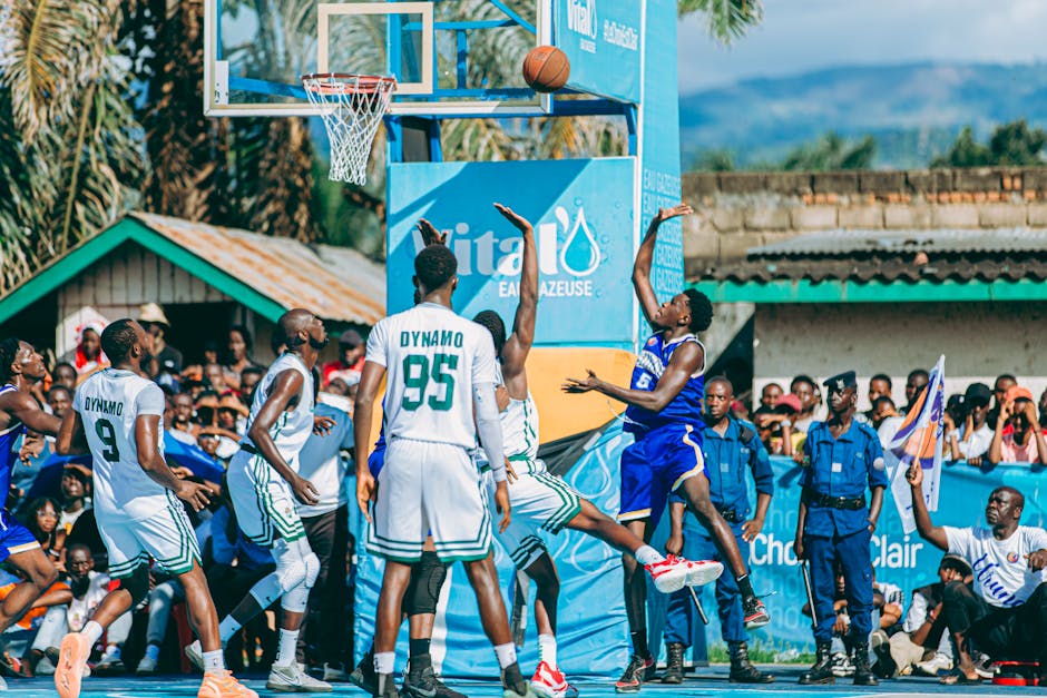 Dynamic outdoor basketball game with players taking a shot and spectators in the background.