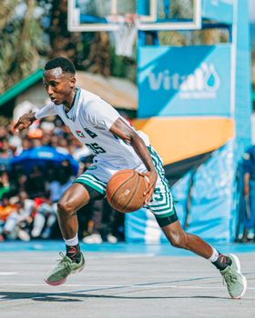 A young male athlete dribbles in an energetic outdoor basketball match.