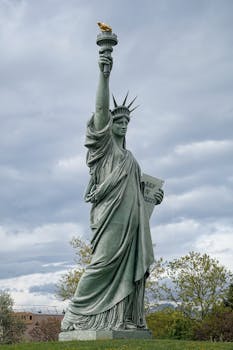 The Statue of Liberty standing tall against a backdrop of cloudy skies with a bird perched on the torch.