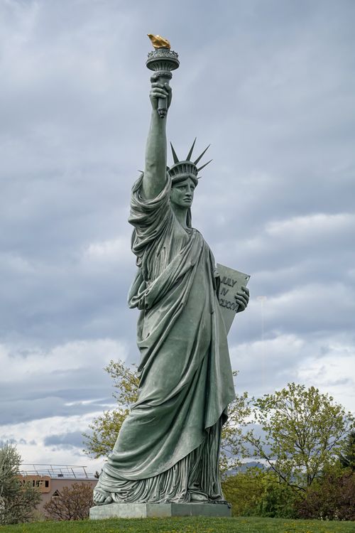 Free The Statue of Liberty standing tall against a backdrop of cloudy skies with a bird perched on the torch. Stock Photo