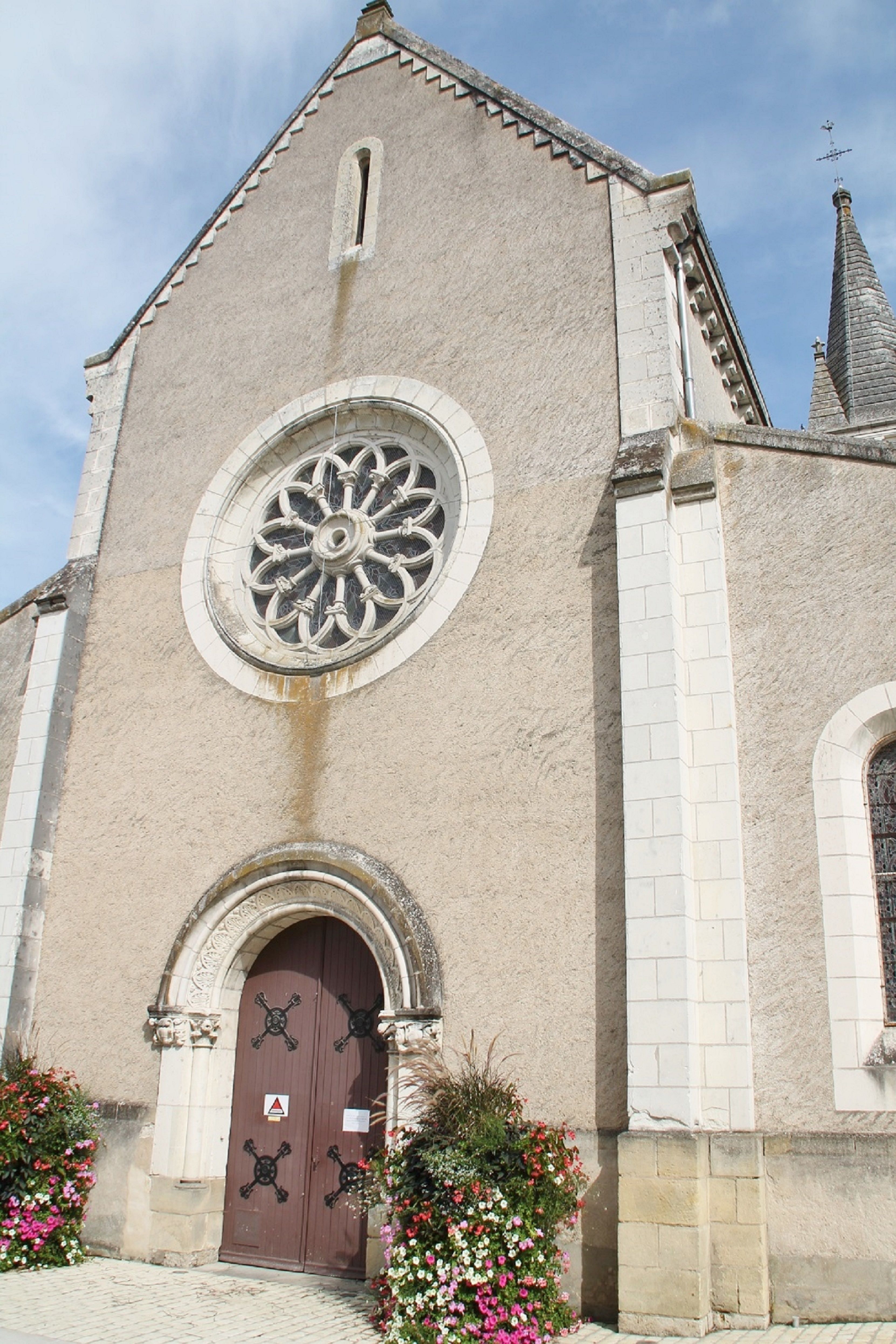A classic stone church facade with a circular stained glass window in Monts, France.
