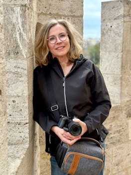 Smiling woman photographer leaning against stone wall, holding camera in Valencia.