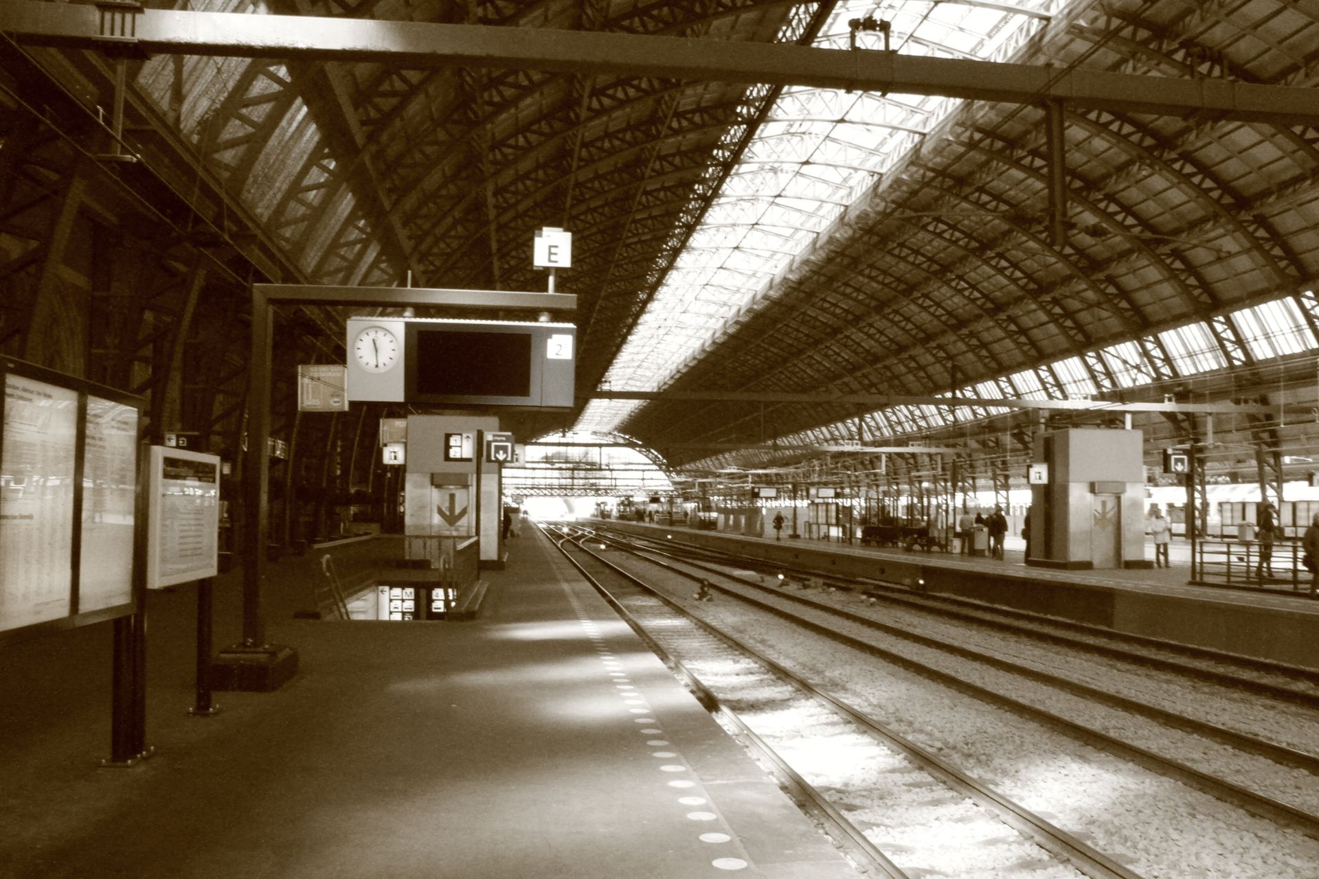 Sepia-toned image of a spacious train station interior with empty tracks and vaulted roof.