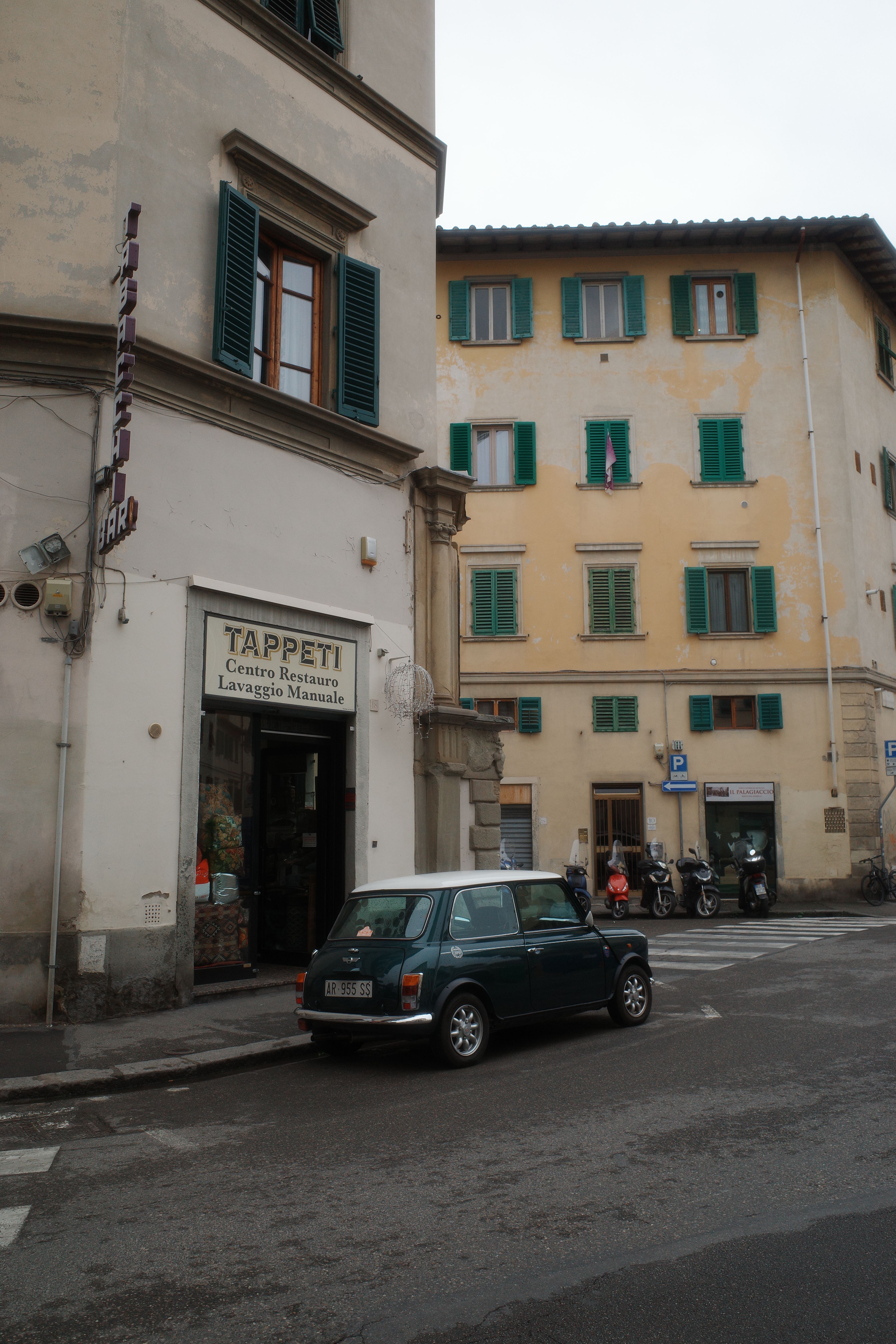 Classic Mini Cooper parked on a European city street surrounded by historic buildings.
