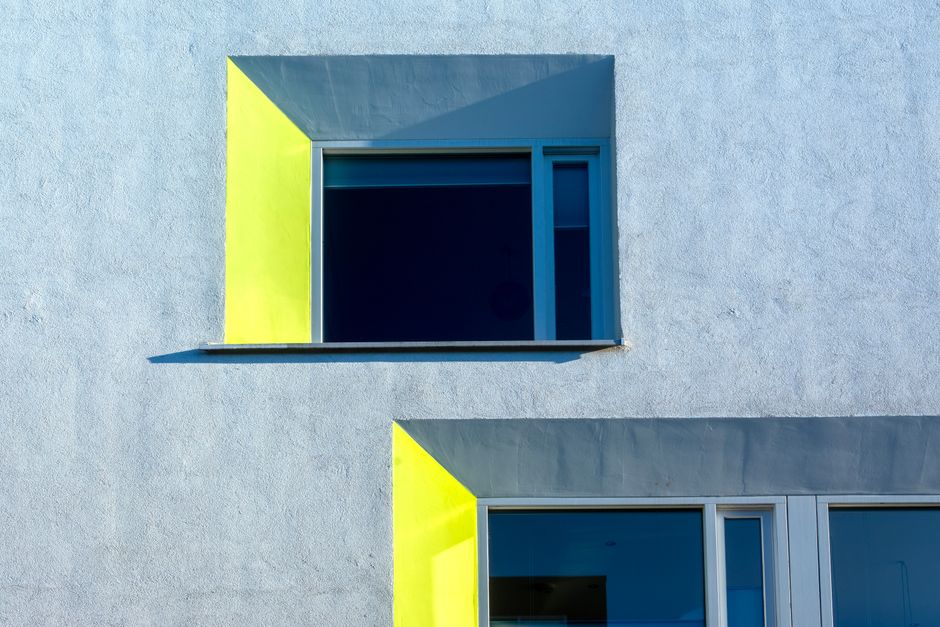 A yellow-framed window with deep blue glass set into a pale concrete facade