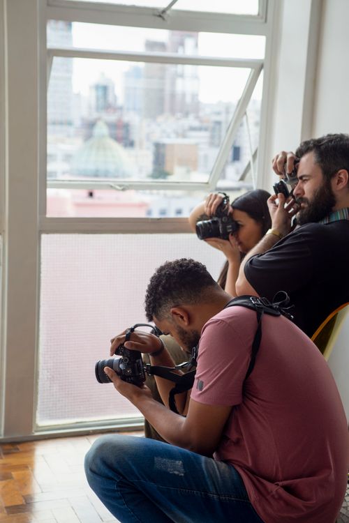 Free Three photographers capturing images in a bright studio with a city view. Stock Photo