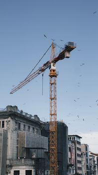 A tower crane stands tall on a construction site amidst old buildings and a clear blue sky.