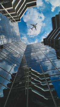 Dynamic view of skyscrapers and an airplane flying above in vibrant blue sky.