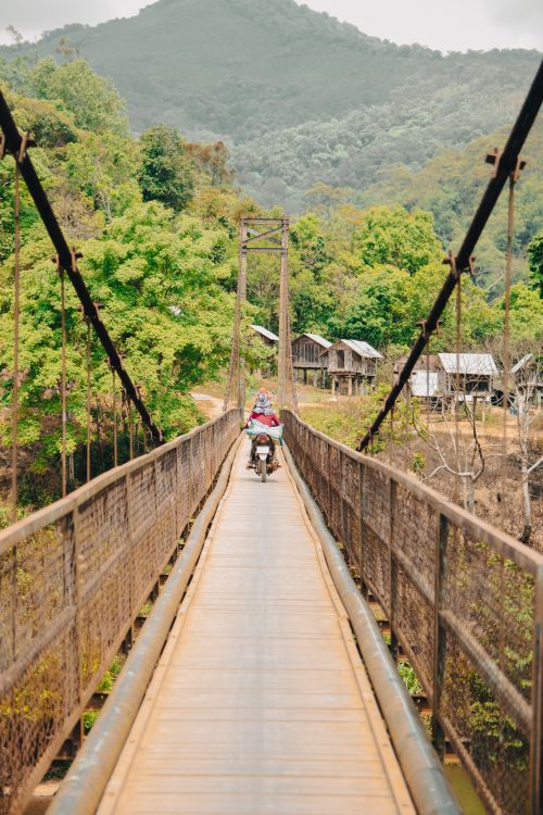 Free Rider on a motorcycle crosses a picturesque suspension bridge in Gia Lai, Vietnam. Stock Photo