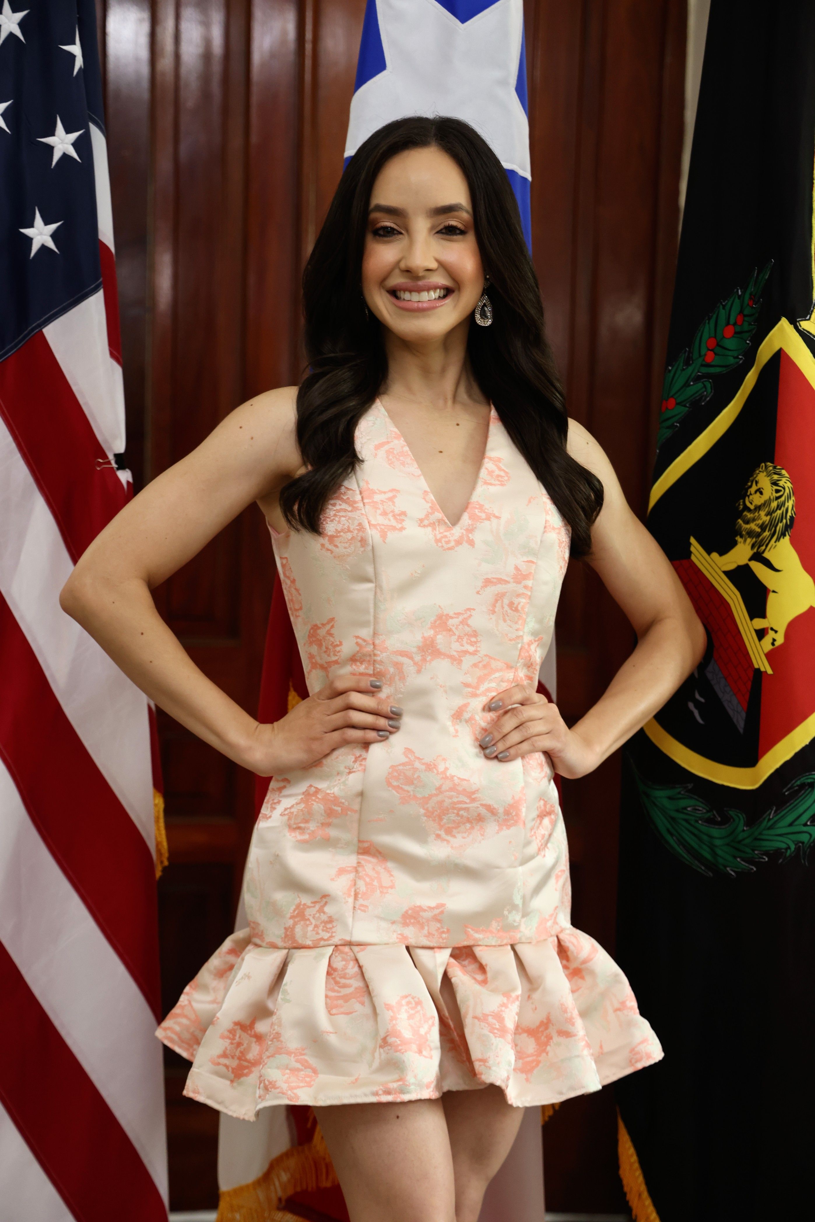 A smiling woman poses confidently near flags indoors, exuding elegance.