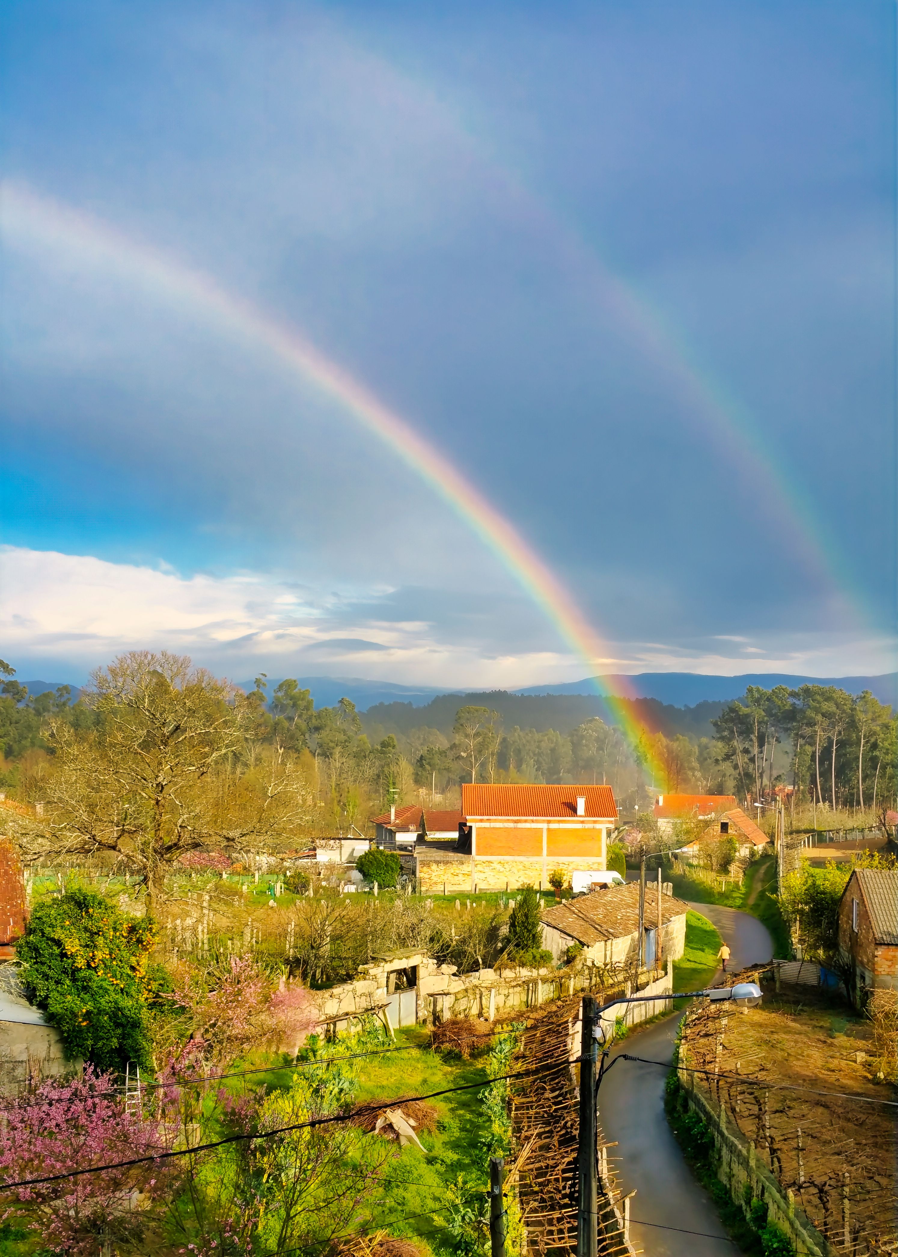 Double rainbow arches over scenic landscape in Salceda de Caselas, Spain under a cloudy sky.