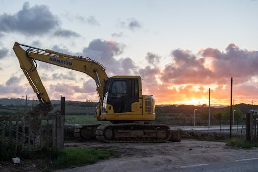 A yellow excavator on a construction site during a vibrant sunset, showcasing industrial work and scenic beauty.