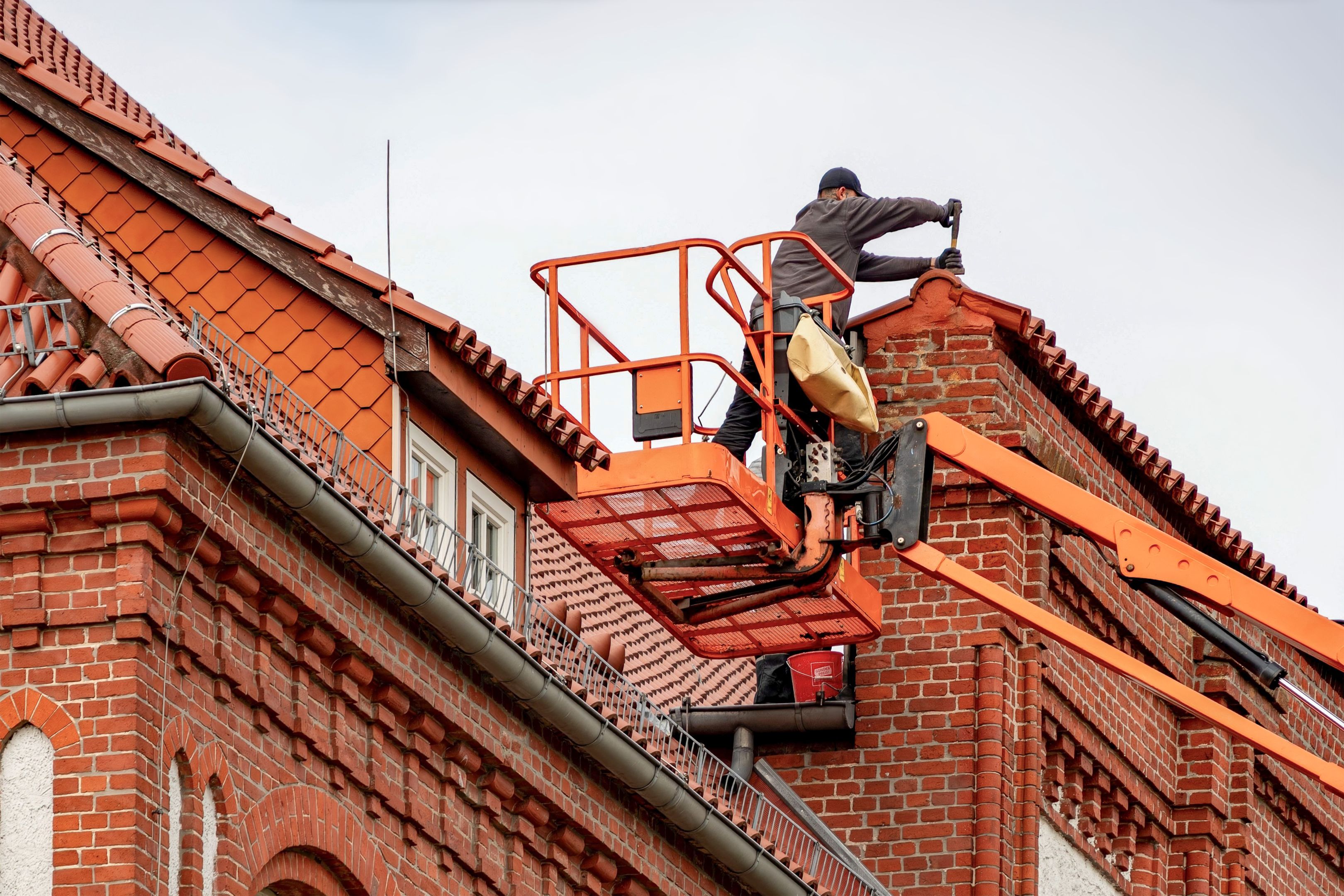 Roofer in a cherry picker conducting maintenance on a building with a tiled roof in Leicestershire