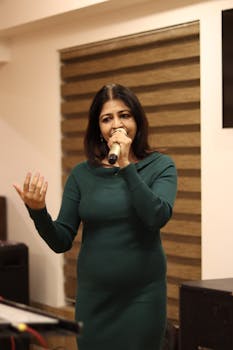 A woman in a green dress sings into a microphone during an indoor event.