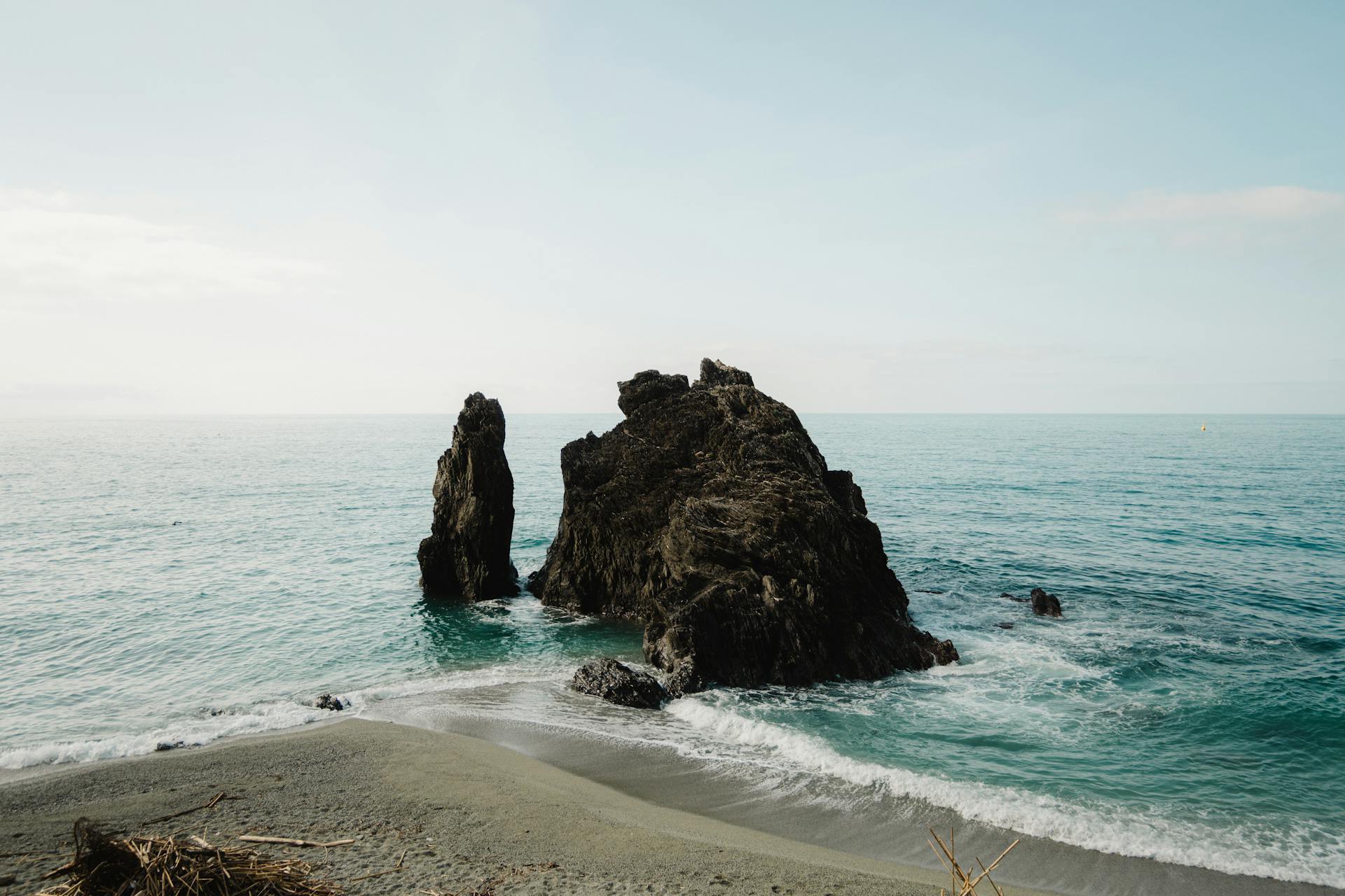 Peaceful coastal scene with large rock formation and blue ocean waves.