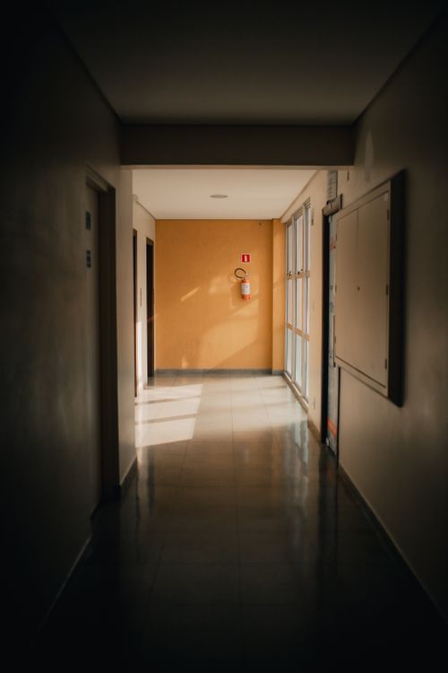 Free A quiet, dimly lit hallway with sunlight streaming through windows, casting shadows. Stock Photo