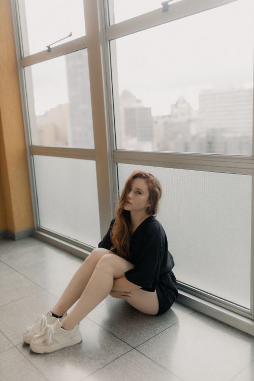Free Young woman sitting by a large window with city view. Stock Photo