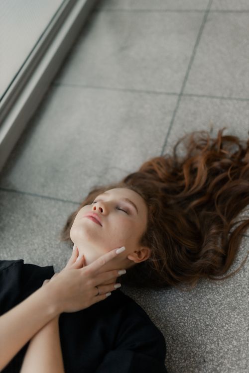 Free Young woman with long red hair lying peacefully on a stone floor inside a building. Stock Photo