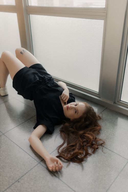 Free A young woman in black clothing poses on the floor indoors, showcasing her long hair. Stock Photo