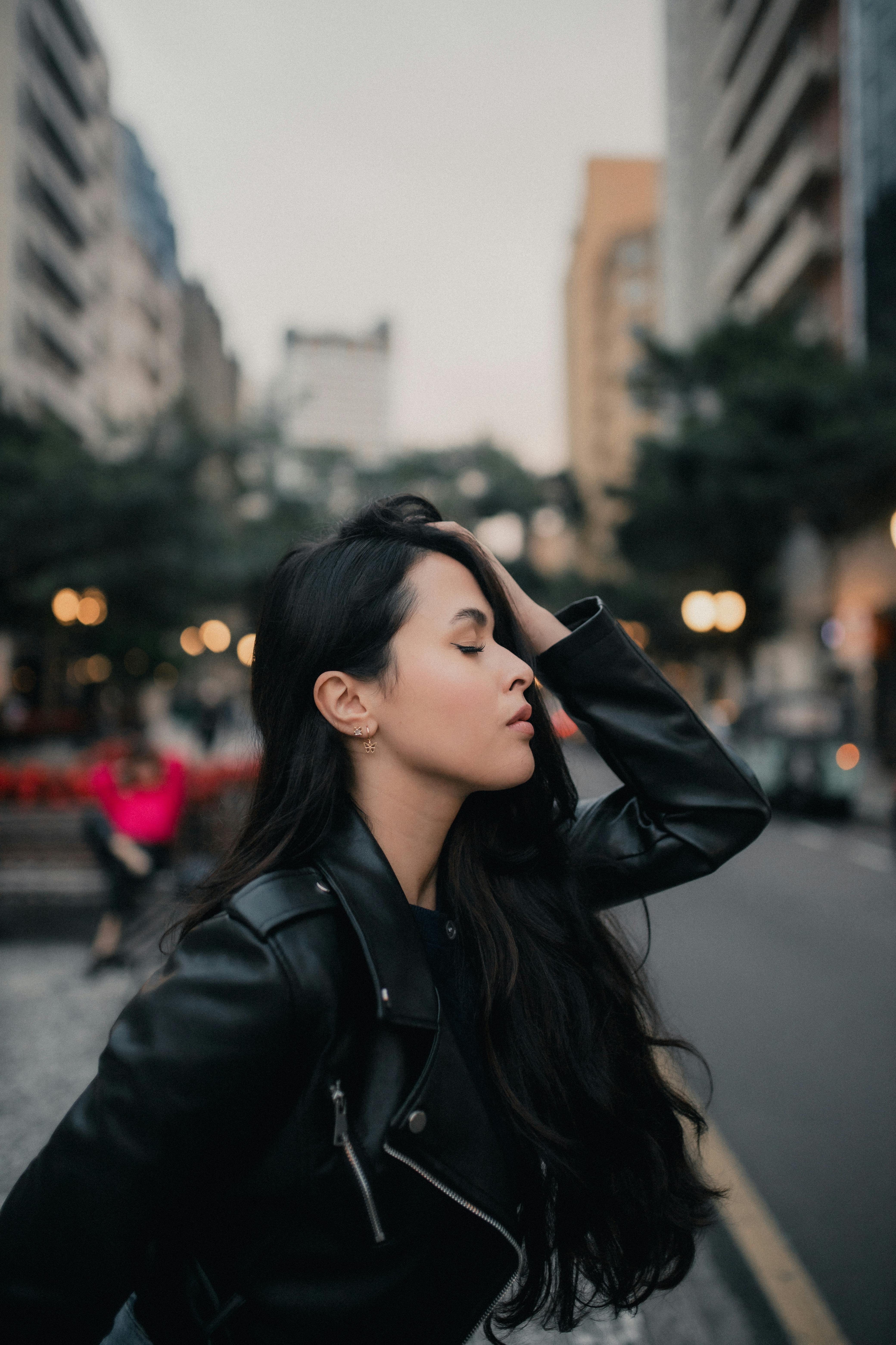 Elegant woman in a leather jacket poses amidst urban architecture, showcasing metropolitan style.