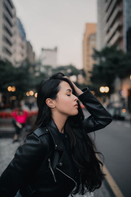 Elegant woman in a leather jacket poses amidst urban architecture, showcasing metropolitan style.