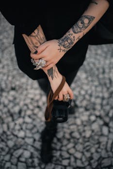 Close-up of tattooed arms holding a camera on a cobblestone street. Artistic and edgy vibe.