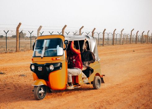 Vibrant tuk-tuk with passengers traversing a dusty road, showcasing rural transportation vibes.